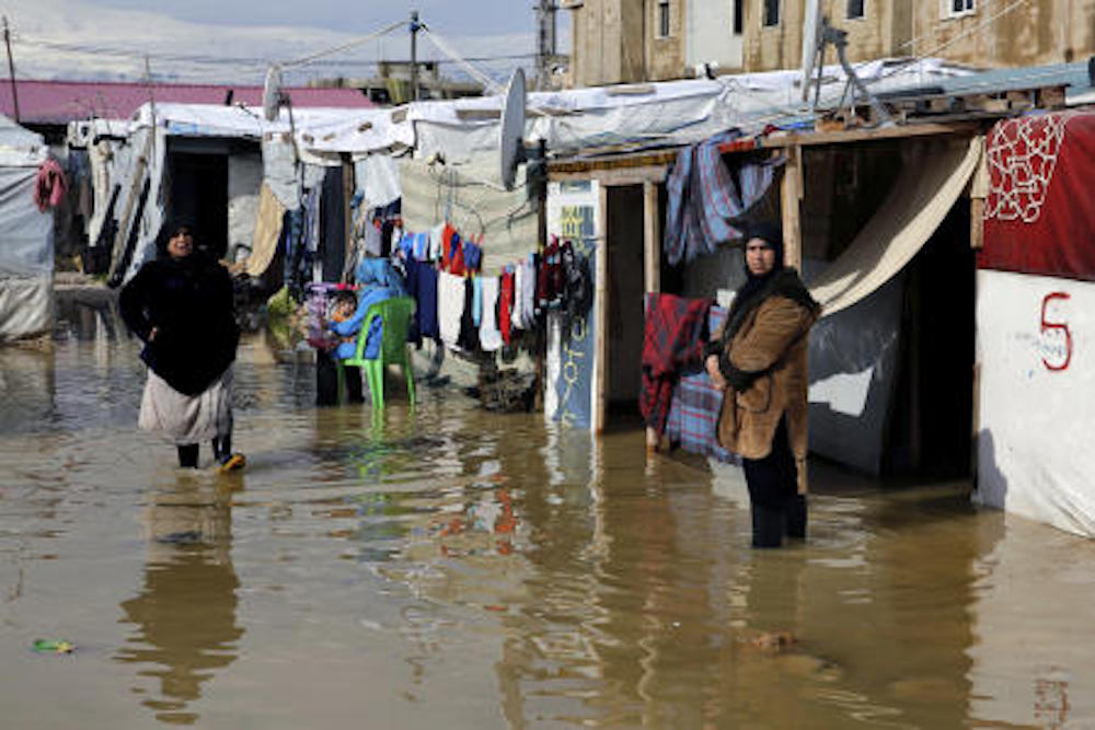 Syrian refugees stand in a pool of mud and rain water at a refugee camp, in the town of Bar Elias. (AP)