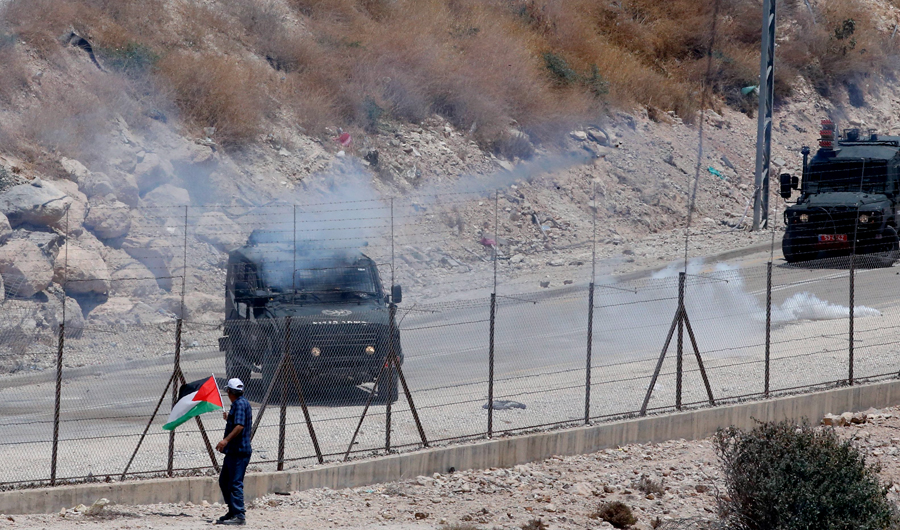 A Palestinian protester waving the national flag as an Israeli military vehicle fires teargas from behind a fence during a demonstration in West Bank. (AFP)