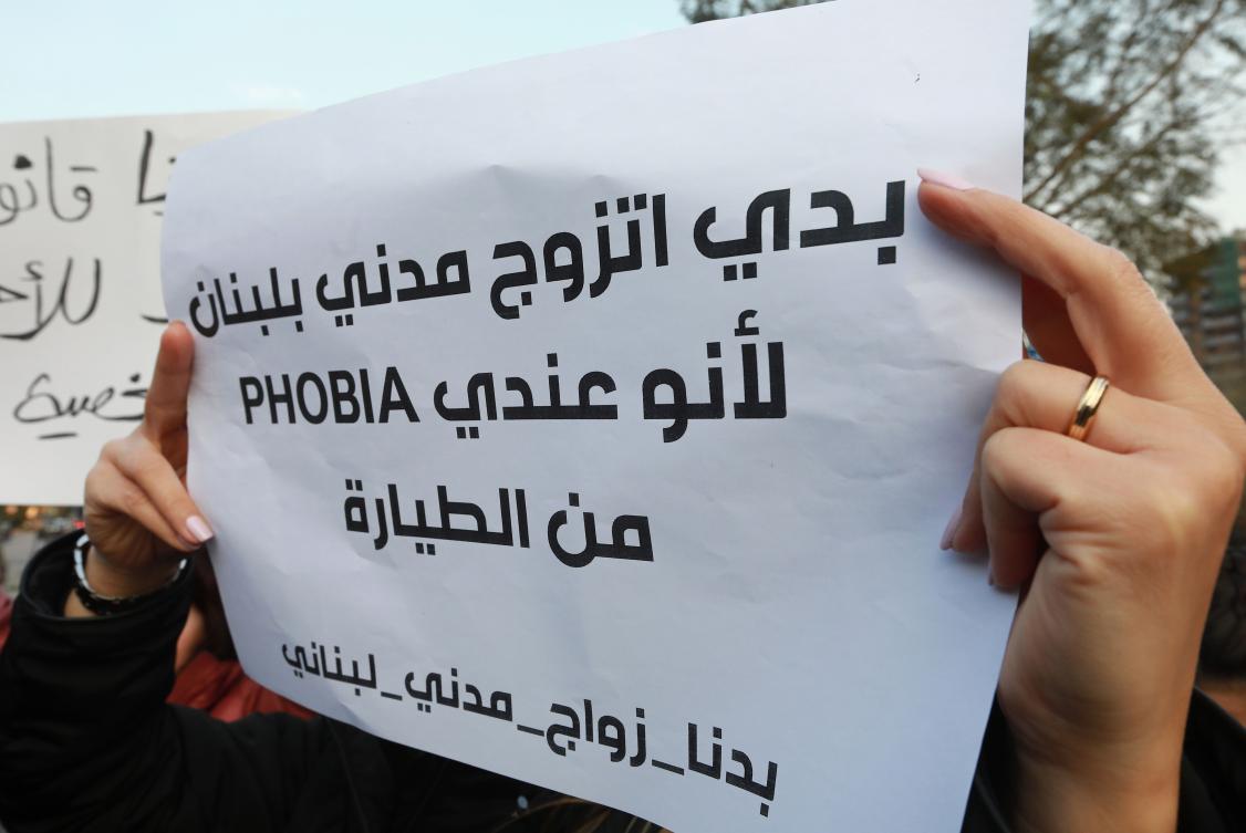 Lebanese demonstrators carry placards during a gathering against the ongoing ban on civil unions outside the Ministry of Interior in the capital Beirut on February 23, 2019. Arabic writing on placard reads:"I want civil marriage in Lebanon because I have a phobia of flying." (AFP)