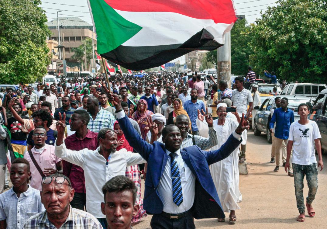 A man flashes the victory gesture while waving a Sudanese national flag during a mass demonstration near the presidential palace in the capital Khartoum on September 12, 2019, calling for the appointment of a new permanent chief of judiciary and prosecutor general. (AFP)