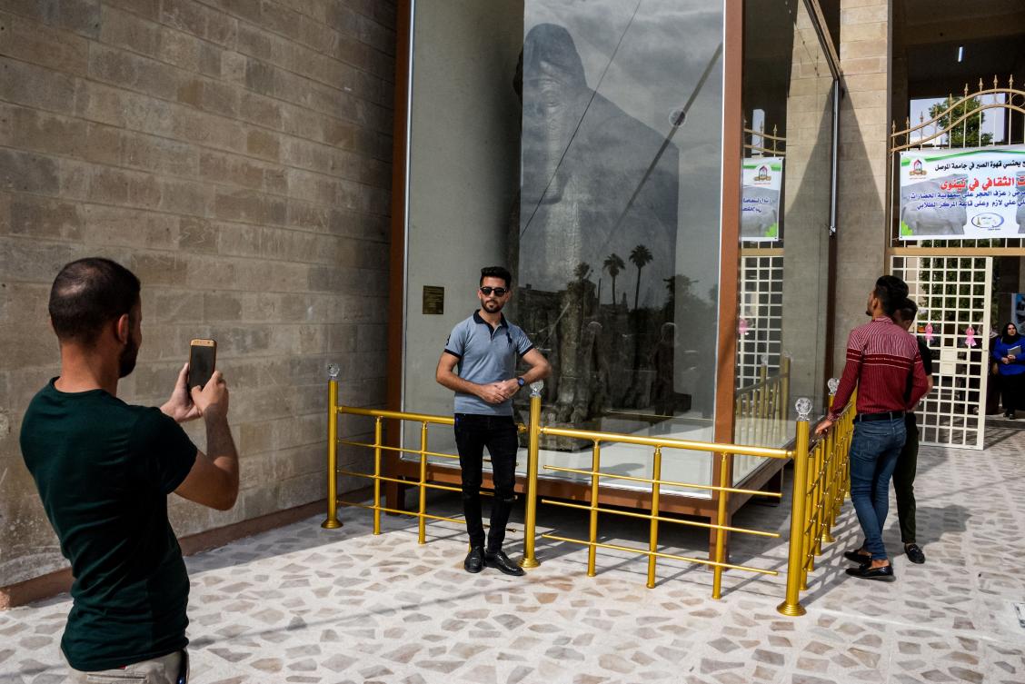 A man poses for a picture with a replica of a "lamassu", an Assyrian protective deity depicted with a human head, the body of a lion, and bird wings, on the day of its unveiling at the University of Mosul in the northern Iraqi city on October 24, 2019. (AFP)