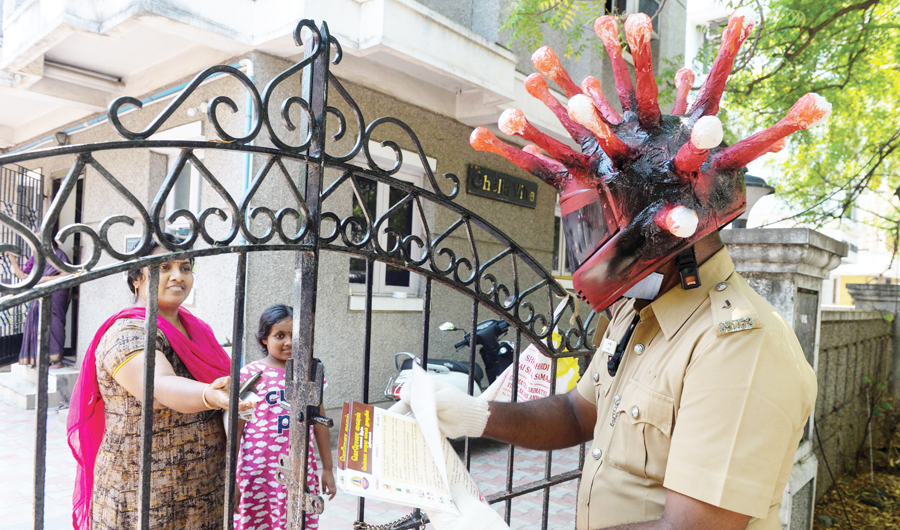 A policeman wearing a a coronavirus helmet distributes pamphlets to raise awareness about the COVID-19 at a residential area in Chennai on Sunday. (AFP)