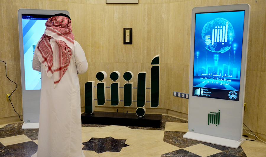 A Saudi Interior Ministry employee stands in front of a screen displaying the Absher mobile app logo at the ministry in Riyadh on February 19, 2019, about the Absher mobile app. (AFP)