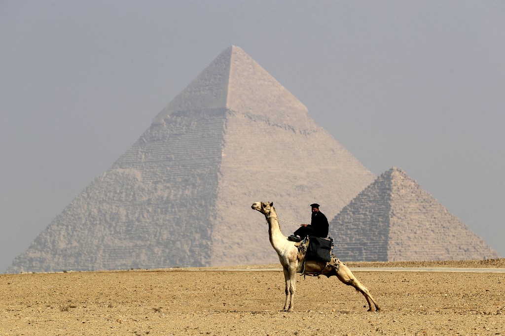 A mask-clad Egyptian policeman rides a camel in front of the Giza Pyramids on the southwestern outskirts of the Egyptian capital Cairo, on December 18, 2020. (File/AFP) 