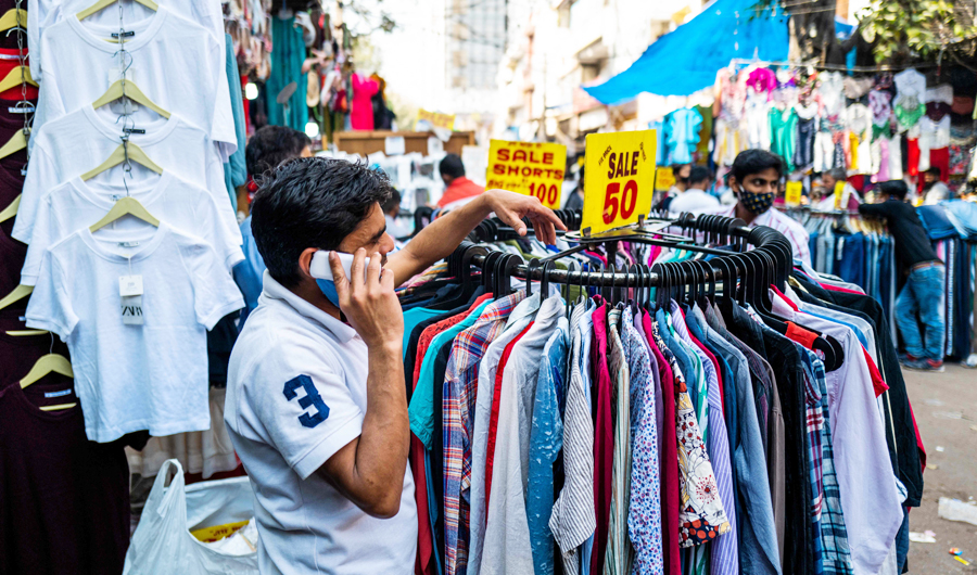 A vendor speaks on his mobile phone as he waits for customers displaying clothing in front of a store in a market in New Delhi on February 23, 2021. (AFP)