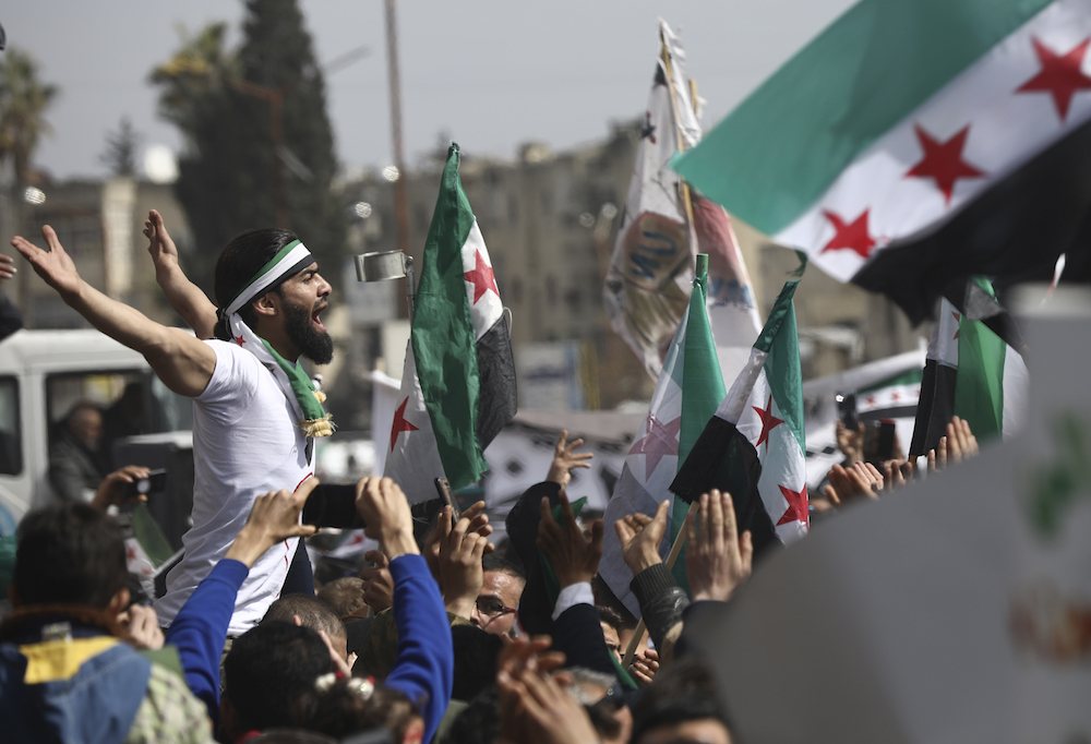 An anti-Syrian government protester shouts slogans as others wave revolutionary flags, to mark 10 years since the start of a popular uprising against President Bashar Assad’s rule, in Idlib, northwest Syria, Monday, Mar. 15, 2021. (AP)