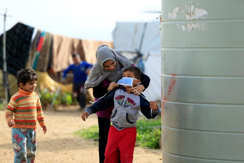 A Syrian refugee woman puts a face mask on a boy as a precaution against the spread of coronavirus, Al-Wazzani, southern Lebanon, March 14, 2020. (Reuters)