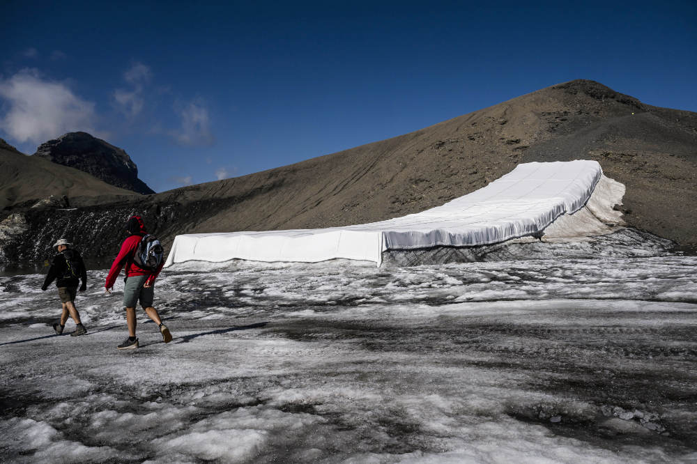Hikers walk in front of snow from the last winter season covered with blankets to prevent it from melting due to global warming at the "Glacier 3000" alpine resort, Switzerland, Thursday, July 28, 2022. (AP)
