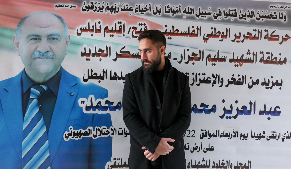 Palestinian nurse Elias al-Ashqar stands by a billboard bearing an obituary for his father Abdel Aziz, on February 24, 2023, who died during an Israeli raid in Nablus in the occupied West Bank two days earlier. (AFP)