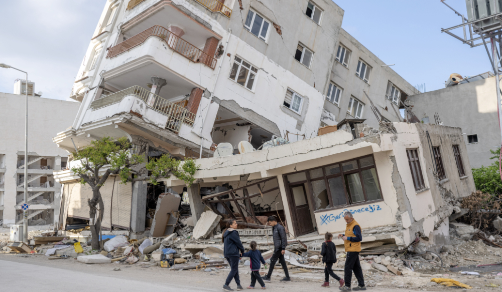 كنان سيفي وعائلته يتجمعون أمام منزلهم المدمر وعليهم كتابات على الجدران "سنعود"في هاتاي في 28 مارس 2023 ، بعد زلزال بقوة 7.8 درجة ضرب في 6 فبراير 2023 في جنوب شرق تركيا.  (أ ف ب)