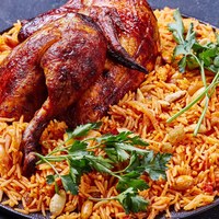 The national Saudi Arabian dish chicken kabsa with roasted chicken quarter and almonds, raisins, garlic on a black plate on a dark concrete background, horizontal orientation, close-up