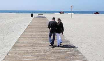 A couple hugs as they walk down a boardwalk on a mostly deserted Santa Monica beach Sunday, March 29, 2020, in Los Angeles. (AP)
