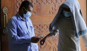 A worshipper covered by his prayer carpet and wearing a mask to curb the spread of the coronavirus has his temperature measured as he enters Al- Jaffali mosque, Jeddah. (AP)