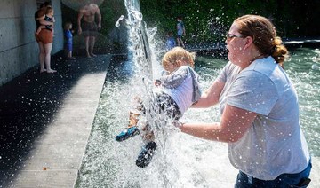 A woman holds a young child under a waterfall at a park in Washington, DC, on June 28, 2021, as a heatwave moves over much of the United States. (AFP)
