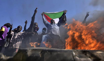 A man holds a Sudanese national flag before flames at a barricade as people protest against the military coup in Sudan, in "Street 60" in the east of capital Khartoum on November 13, 2021. (AFP)