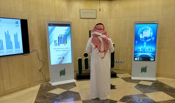 A Saudi Interior Ministry employee stands in front of a screen displaying the Absher mobile app logo at the ministry in Riyadh. 