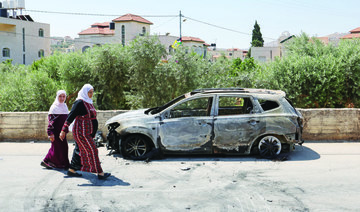 Palestinians walk past a burnt car, which was set on fire by Israeli settlers, near the occupied West Bank city of Ramallah. 