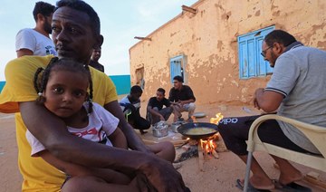 People sit around food cooking on a bonfire at a school that has been transformed into shelter for people displaced by conflict.