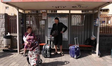 People with their luggage wait at a bus stop in the northern Israeli town of Kiryat Shmona on the border with Lebanon.