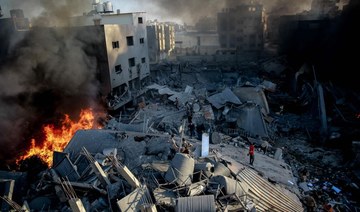 Smoke and fire rise from a levelled building as people gather amid the destruction in the aftermath of an Israeli strike on Gaza