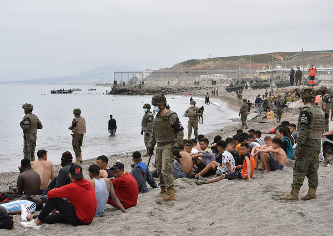 Migrants, including minors, who arrived swimming at the Spanish enclave of Ceuta, rest as Spanish soldiers stand guard on May 18, 2021 in Ceuta. (AFP)