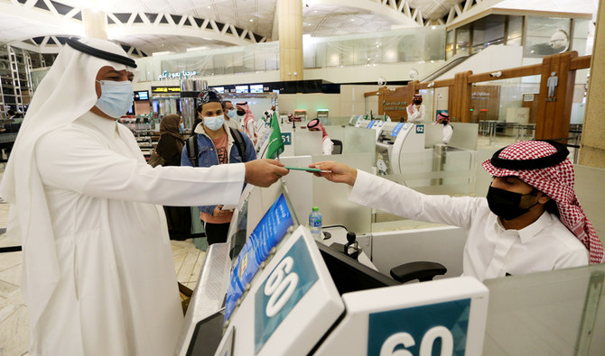 A Saudi man wearing a face mask gets his passport from a Saudi Immigration officer at the King Khalid International Airport in Riyadh, Saudi Arabia. (REUTERS)