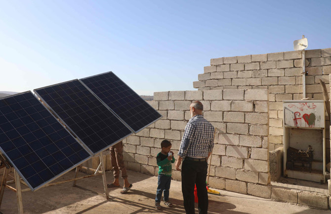 A man and his son stand near a solar panel installed on the rooftop of their house in the village of Killi, in Syria's northwestern Idlib province. (AFP / Aaref Watad)