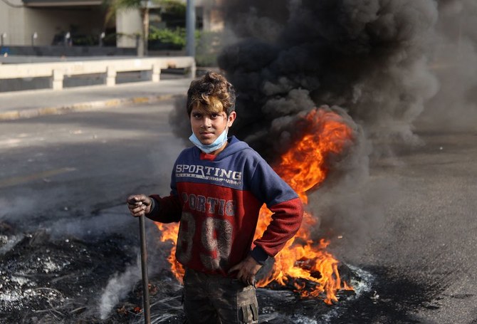 A Lebanese youth stands by burning tyres blocking a road during a protest in the capital Beirut on November 29, 2021, as the country struggles with a deep economic crisis. (AFP)
