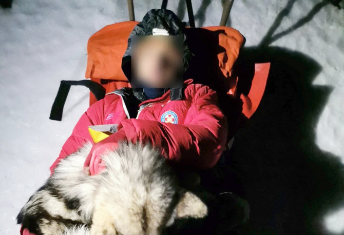 This undated photograph released by Croatian Mountain Rescue Service (HGSS) on January 4, 2022, shows the dog "North" lying on a mountaineer as they are rescued by HGSS servicemen on the mountain of Velebit. (AFP)