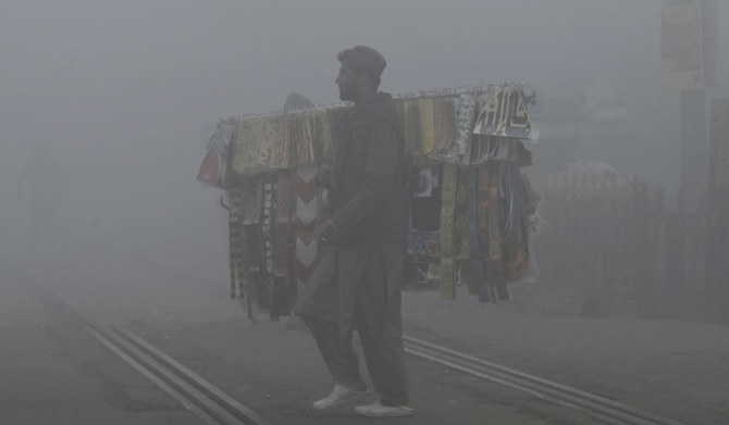 A vendor crosses a rail track amid smoggy and foggy conditions early in the morning in Lahore on January 3, 2023. (AFP)