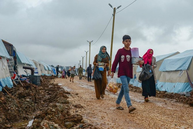 People carry food on a muddy path next to tents donated by Turkish Turk Kizilay humanitarian organization.