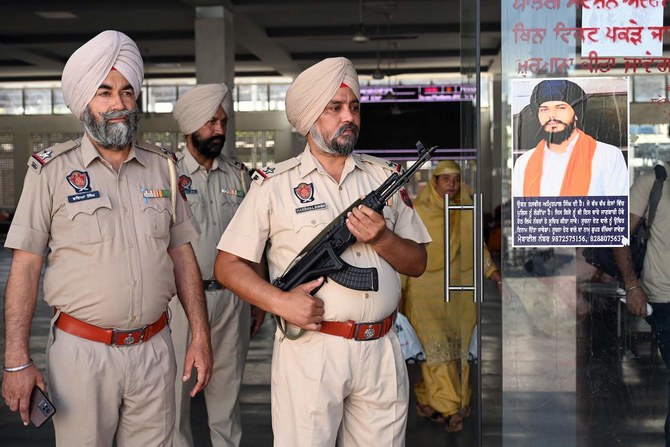 Punjab police stand guard beside Amritpal Singh’s poster at a railway station in Amritsar. (File/AFP)