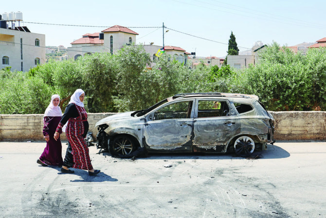 Palestinians walk past a burnt car, which was set on fire by Israeli settlers, near the occupied West Bank city of Ramallah. 