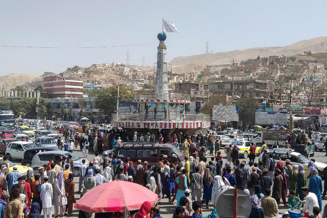 A Taliban flag is seen on a plinth with people gathered around the main city square at Pul-e-Khumri on August 11, 2021 after Taliban fighters captured Pul-e-Khumri, the capital of Baghlan province about 200 km north of Kabul. (Photo by AFP)