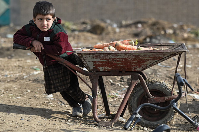 An Afghan child rests next to a wheelbarrow filled with carrots in Balkh, northwest of Mazar-i-Sharif on Dec. 22, 2021. (Photo by Mohd Rasfan / AFP) 