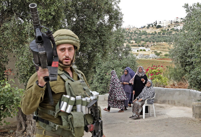 Palestinian women stand and sit by as Israeli security forces inspect the in the area of Dora. (File/AFP)