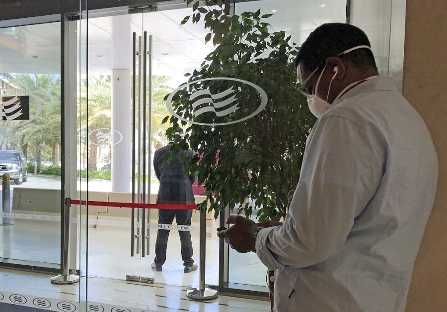 A mask-clad man uses his mobile phone while standing at the entrance of the Crowne Plaza hotel in Yas Island Abu Dhabi, where two Italian cyclists participating in the UAE Tour tested positive for COVID-19 coronavirus disease which prompted the cancellation of the cycling event, on February 28, 2020. (File/AFP)